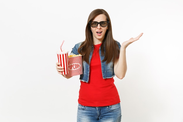 Portret van jonge geïrriteerde vrouw in 3D-bril kijken naar filmfilm, met emmer popcorn en plastic beker frisdrank of cola, spreidende hand geïsoleerd op een witte achtergrond. Emoties in bioscoopconcept.