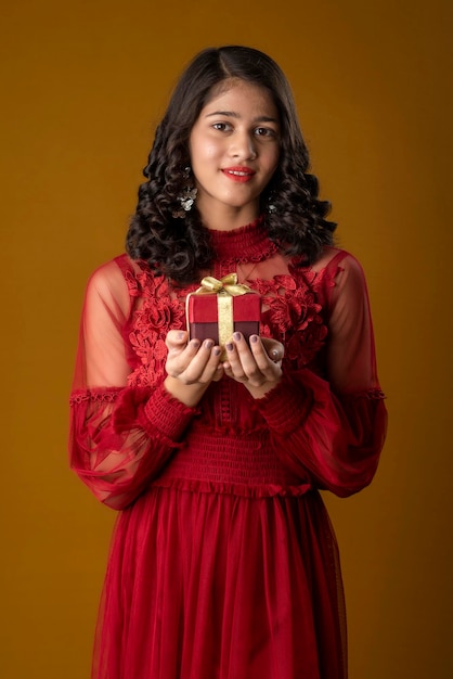 Portret van jonge gelukkig lachend meisje houden en poseren met geschenkdoos op bruine achtergrond