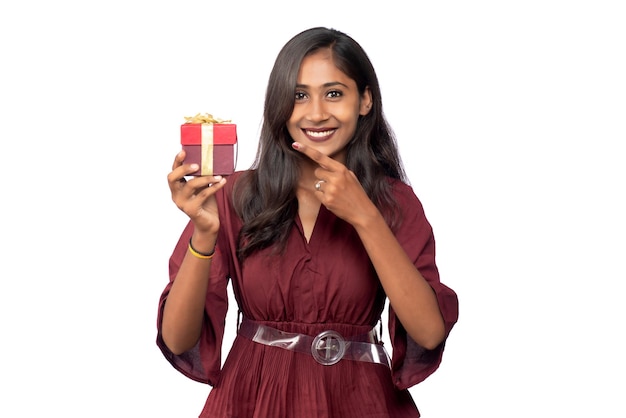 Portret van jonge gelukkig lachend meisje in rode jurk houden en poseren met geschenkdoos op witte achtergrond
