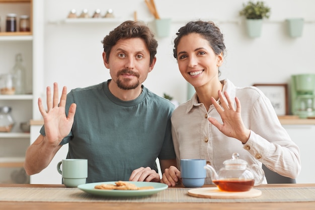 Portret van jonge gelukkige paar ontbijten en glimlachen zittend aan tafel in de keuken