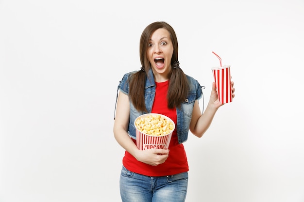 Portret van jonge geschokt mooie vrouw in casual kleding kijken naar film film, emmer popcorn en plastic beker frisdrank of cola geïsoleerd op een witte achtergrond. Emoties in bioscoopconcept.