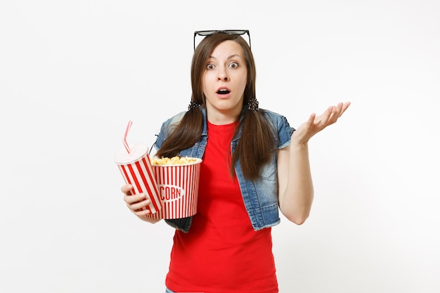 Portret van jonge geschokte vrouw in 3D-bril kijken naar filmfilm, met emmer popcorn, plastic beker frisdrank of cola spreidende handen geïsoleerd op een witte achtergrond. Emoties in bioscoopconcept.