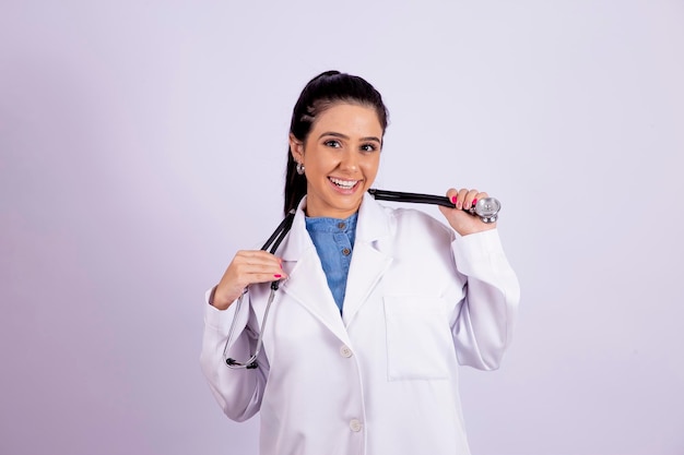 Portret van jonge glimlachende vrouwelijke arts die camera bekijkt die een stethoscoop houdt