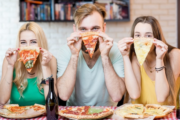 Portret van jonge grappige vrienden, nonchalant gekleed in kleurrijke t-shirts met een stuk pizza thuis