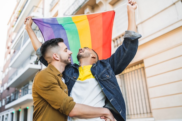 Portret van jonge homo paar omarmen en tonen hun liefde met Regenboogvlag in de straat. LGBT en liefde concept.