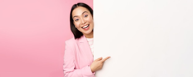 Portret van jonge Japanse zakenvrouw corporate dame in pak wijzend op de muur met grafiek met diagram of advertentie op lege kopie ruimte roze achtergrond