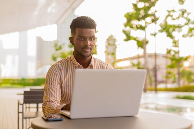 Portret van jonge knappe Afrikaanse zakenman die laptopcomputer met behulp van bij coffeeshop