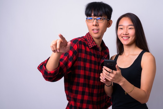 Portret van jonge knappe Aziatische man en jonge mooie Chinese vrouw samen en verliefd tegen witte muur