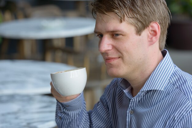 Portret van jonge knappe blonde zakenman ontspannen in de coffeeshop buitenshuis