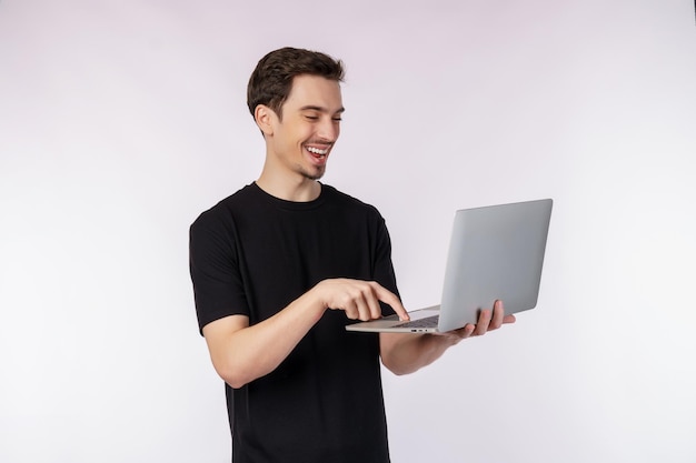 Portret van jonge knappe glimlachende man met laptop in handen typen en browsen op webpagina's geïsoleerd op een witte achtergrond