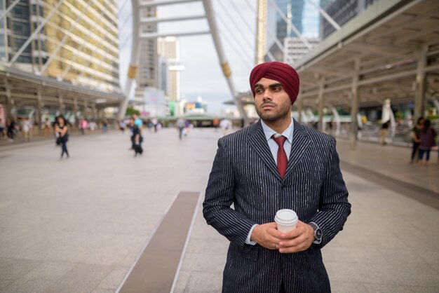 Portret van jonge knappe Indiase Sikh zakenman tulband dragen tijdens het verkennen van de stad Bangkok, Thailand