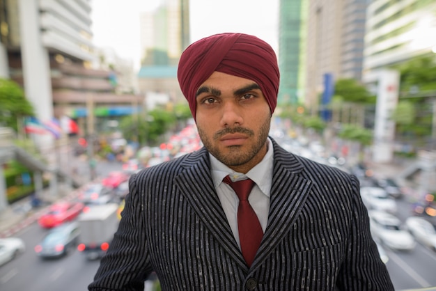 Portret van jonge knappe Indiase Sikh zakenman tulband dragen tijdens het verkennen van de stad Bangkok, Thailand