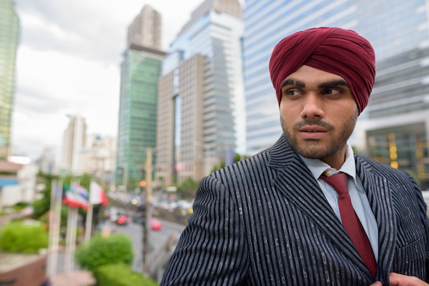 Portret van jonge knappe Indiase Sikh zakenman tulband dragen tijdens het verkennen van de stad Bangkok, Thailand