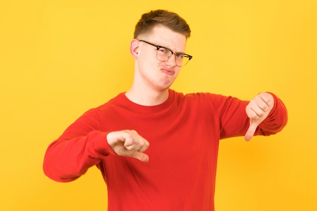 Portret van jonge knappe teleurgestelde kerel in rode sweater met neer duimen