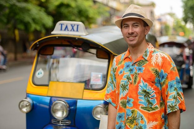 Portret van jonge knappe toeristenmens met tuk tuk als lokaal openbaar vervoer in de stad van Bangkok