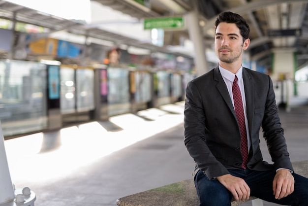 Portret van jonge knappe zakenmanzitting bij treinstation
