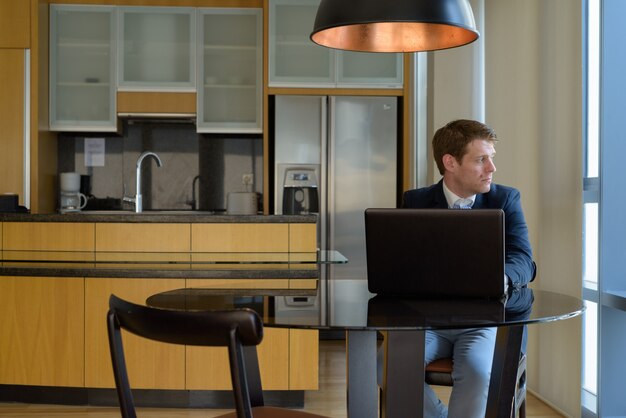 Portret van jonge knappe zakenmanzitting in de eetkamer dichtbij de keuken