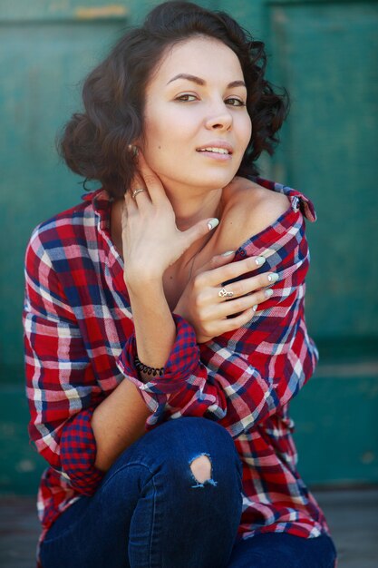 Portret van jonge krullende vrouw op groene muur. Glimlachend en emotioneel meisje in jeans en rood shirt op de stadsstraat. Leuke jonge vrouw in openlucht in zonnige dag