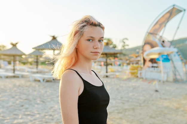 Portret van jonge lachende blonde tiener in zwarte top op het strand