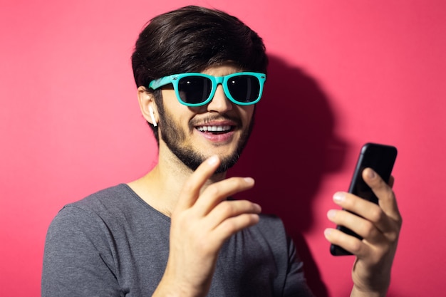 Portret van jonge lachende man met behulp van smartphone en draadloze oortelefoons