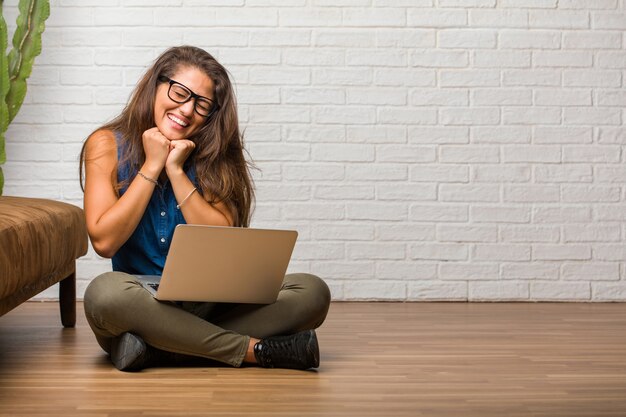 Portret van jonge latijns-vrouw zittend op de vloer erg blij en opgewonden, het verhogen van de armen, het vieren van een overwinning of succes, het winnen van de loterij. een laptop vasthouden.