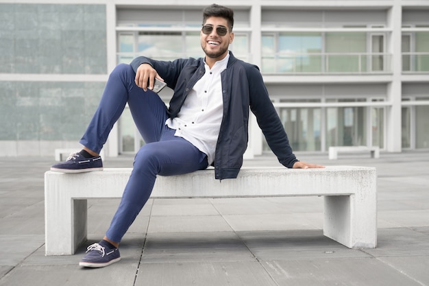 Portret van jonge man in stijlvolle zonnebril poseren in de buurt van modern gebouw