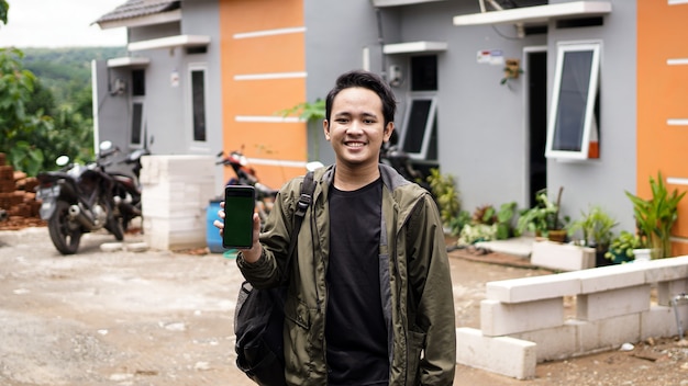 Portret van jonge mannen die voor hun nieuwe huis staan en greensreen telefoon houden