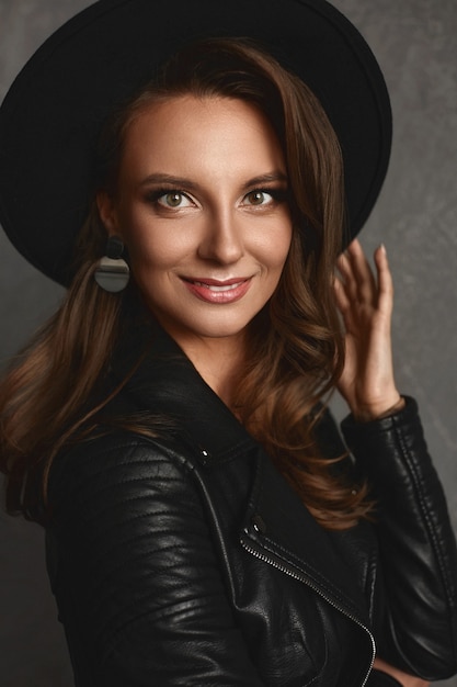 Portret van jonge modelvrouw met lichte make-up en perfecte huid in een zwarte trendy hoed en leerjasje