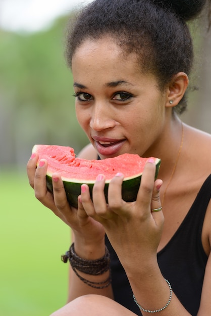 Portret van jonge mooie Afrikaanse vrouw met Afro haar ontspannen in het park buiten