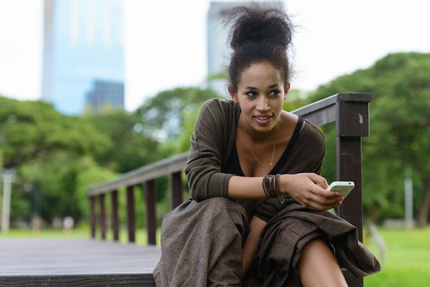 Portret van jonge mooie Afrikaanse vrouw met Afro haar ontspannen in het park buiten