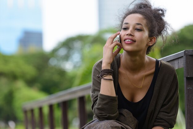 Portret van jonge mooie Afrikaanse vrouw met Afro haar ontspannen in het park buiten