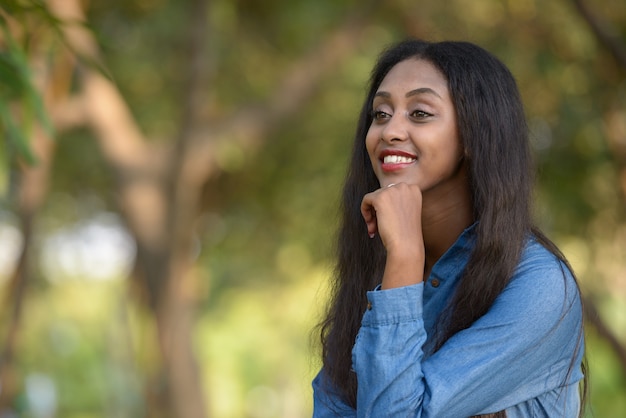 Portret van jonge mooie Afrikaanse vrouw ontspannen in het park buiten