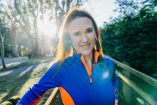 Portret van jonge mooie atleet vrouw verlicht met flare camera kijken bij zonsondergang in de lente of zomer in een bosrijk park. bedrijfsimago concept. vrouw en sport