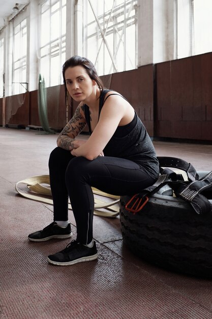 Portret van jonge mooie atletische vrouw met getatoeëerde arm zittend op band na cross training training en op zoek