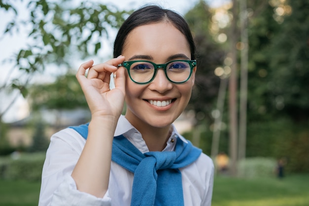 Portret van jonge mooie Aziatische vrouw die oogglazen draagt, camera bekijkt