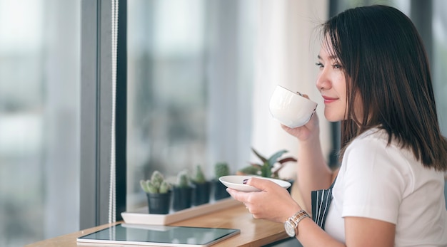 Portret van jonge mooie Aziatische vrouw koffie drinken met geluk zittend in modern café.