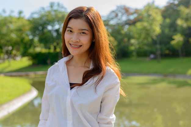 Portret van jonge mooie Aziatische vrouw ontspannen in het park buiten