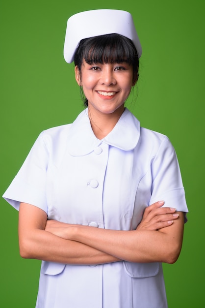 Portret van jonge mooie Aziatische vrouwenverpleegster tegen groene muur