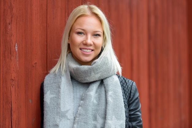 Portret van jonge mooie blonde Scandinavische vrouw tegen rode houten gebouw buitenshuis