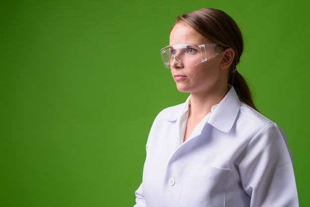 Portret van jonge mooie blonde vrouw arts beschermende bril op groen