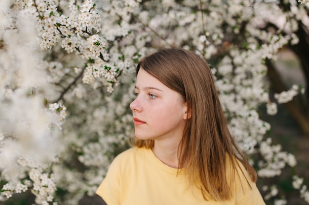 Portret van jonge mooie blonde vrouw in de buurt van bloeiende boom met witte bloemen op een zonnige dag.