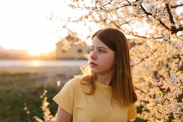 Portret van jonge mooie blonde vrouw in de buurt van bloeiende boom met witte bloemen op een zonnige dag