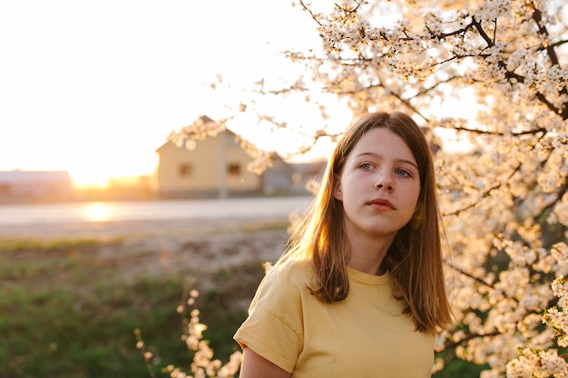 Portret van jonge mooie blonde vrouw in de buurt van bloeiende boom met witte bloemen op een zonnige dag