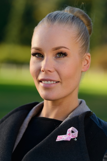 Portret van jonge mooie blonde vrouw met roze lint voor symbool van de voorlichting van borstkanker in het park