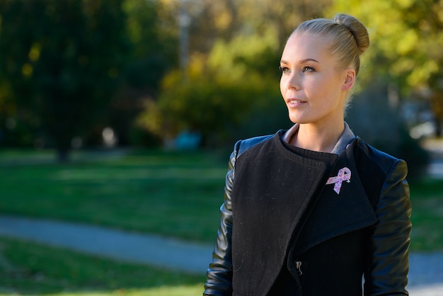 Portret van jonge mooie blonde vrouw met roze lint voor symbool van de voorlichting van borstkanker in het park