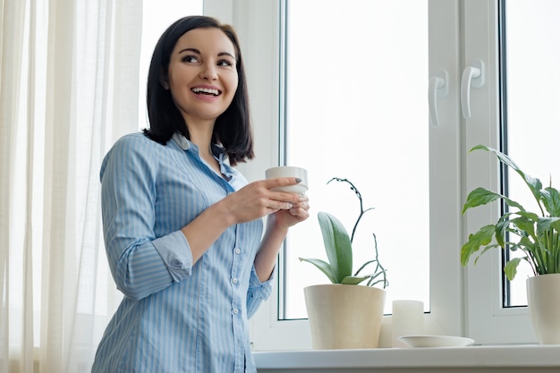 Portret van jonge mooie glimlachende vrouw met kop van koffie