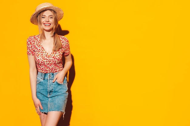 Portret van jonge mooie lachende blonde vrouw in trendy zomerkleren zorgeloze vrouw poseren in de buurt van gele muur in studio Positief model plezier binnenshuis vrolijk en gelukkig In hoed