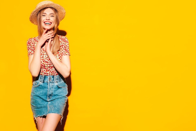 Portret van jonge mooie lachende blonde vrouw in trendy zomerkleren zorgeloze vrouw poseren in de buurt van gele muur in studio Positief model plezier binnenshuis vrolijk en gelukkig In hoed