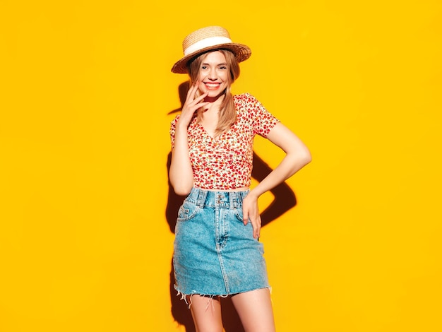 Portret van jonge mooie lachende blonde vrouw in trendy zomerkleren zorgeloze vrouw poseren in de buurt van gele muur in studio Positief model plezier binnenshuis vrolijk en gelukkig In hoed