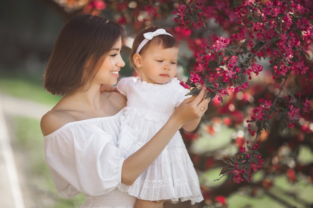 Portret van jonge mooie moeder met haar kleine babymeisje. Sluit nog steeds van liefhebbende familie. Aantrekkelijke vrouw die haar kind in roze bloemen en het glimlachen houdt.